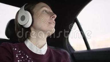 穿着白色上衣和栗色毛衣的棕色头发的漂亮女人坐在车上堵车，和她一起听音乐